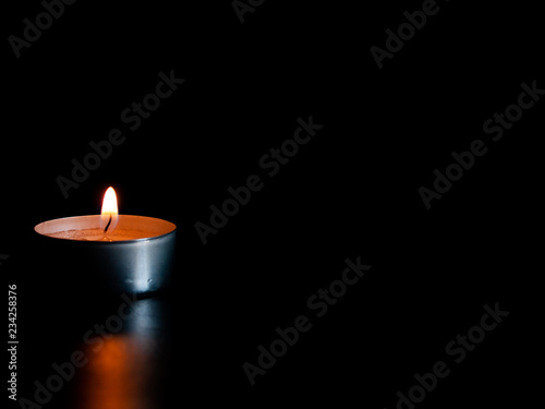 A lighted candle with an orange flame and isolated on a black background