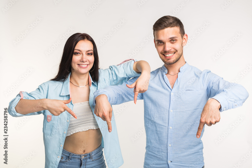 People and gesture concept - young pretty woman and handsome man pointing down over white background People and gesture concept - young pretty woman and handsome man pointing down over white background