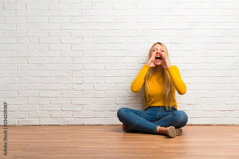 Young girl sitting on the floor shouting with mouth wide open and announcing something