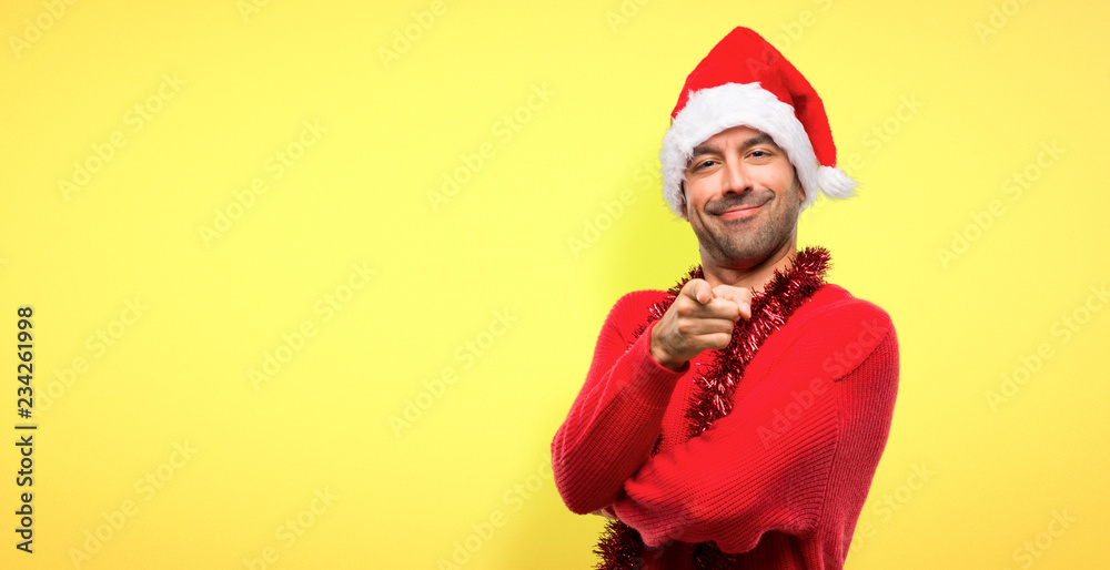 Man with red clothes celebrating the Christmas holidays points finger at you with a confident expression on yellow background