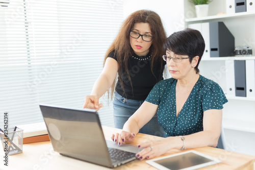 Business people, technology and communication concept - middle-aged woman showing something to another woman on laptop in office © satura_