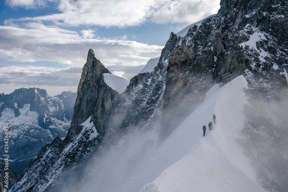 Climbers or alpinist on a knife sharp ridge of an alpine peak or summit of Aiguille du Rochefort. Alpine landscape and adventure climbing ascent in Mont Blanc Massif. Alpinism in high mountains. - obrazy, fototapety, plakaty 