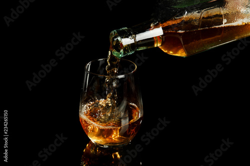 Pouring of whiskey from bottle into glass on black background