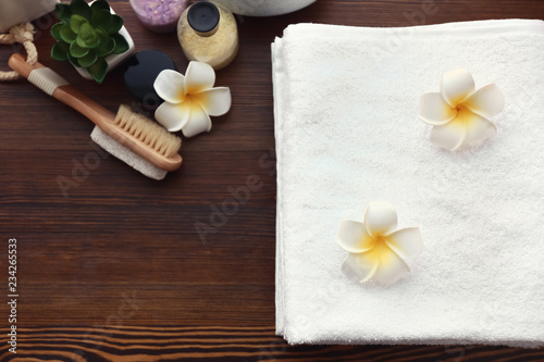 White terry towels with flowers and cosmetics on wooden table indoors