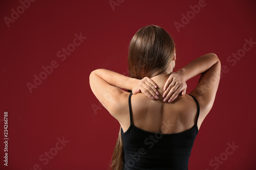 Young woman suffering from neck pain on color background