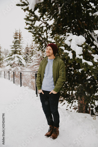 Young Trendy Man in Green Bomber Jacket Enjoying the Winter Snow on a Small Bridge in Colorado