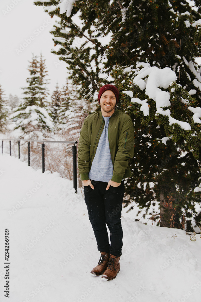 Young Trendy Man in Green Bomber Jacket Enjoying the Winter Snow on a Small Bridge in Colorado