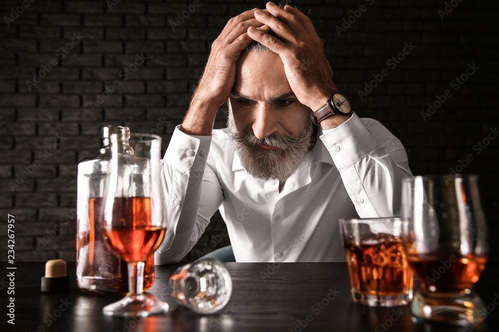 Depressed senior man drinking whiskey at table on dark background Depressed senior man drinking whiskey at table on dark background