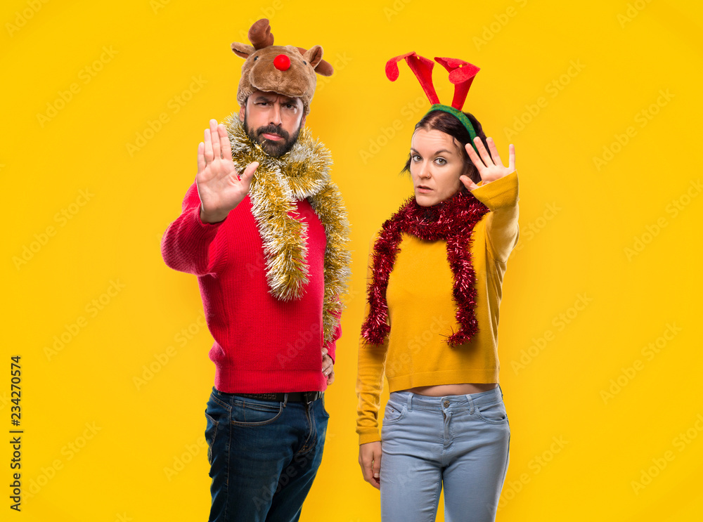 Couple dressed up for the christmas holidays making stop gesture with her hand denying a situation that thinks wrong on yellow background Couple dressed up for the christmas holidays making stop gesture with her hand denying a situation that thinks wrong on yellow background