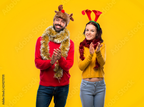 Couple dressed up for the christmas holidays applauding after presentation in a conference on yellow background