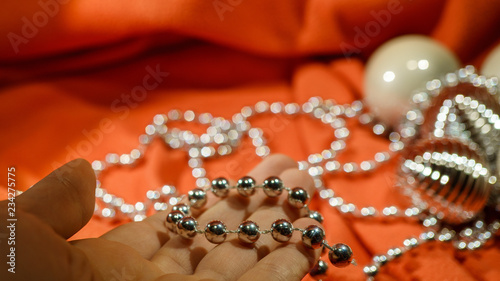 Selective focus on a Caucasian woman hand holding a silver ball garland on a festive red soft background. Winter holiday concept.
