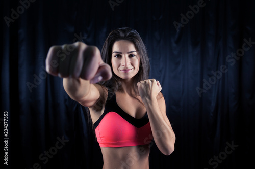 A beautiful brunette in a pink sports top works out a strong punch on a dark background