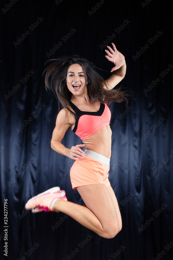 Beautiful brunette in a bright sports form with perfect body jumps on a black background. Selective focus on the face Beautiful brunette in a bright sports form with perfect body jumps on a black background. Selective focus on the face