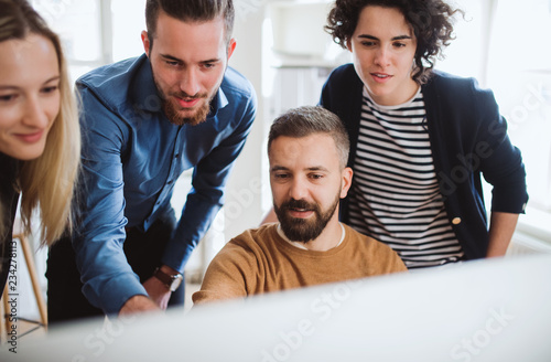 Group of young businesspeople looking at laptop screen in office, discussing issues.