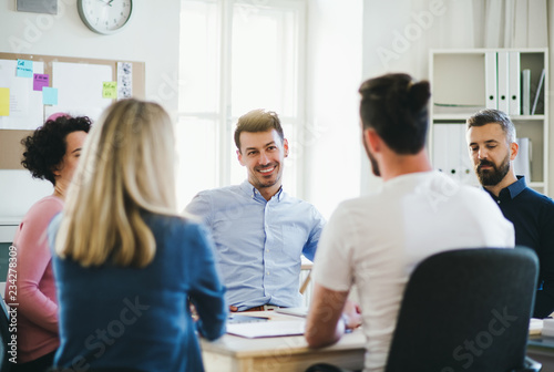 Group of young businesspeople sitting around table in a modern office, having meeting.