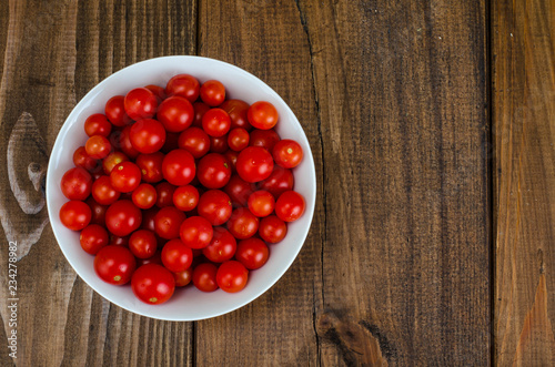 Small red cherry tomatoes in white bowl on wooden background
