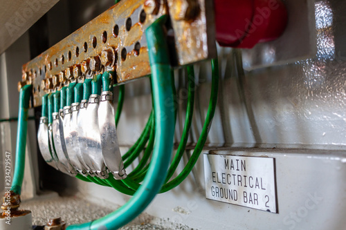 Green electrical ground wires is connected to ground copper terminal bar or earth bonding terminal bar in electrical device and electrical grounding sign near ground bolt for safety system.