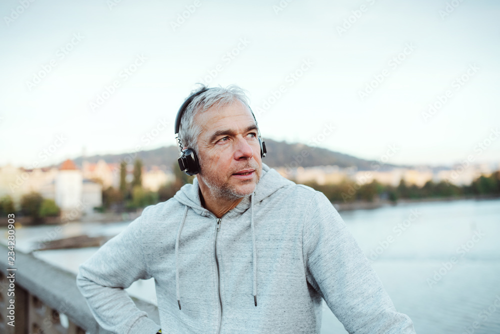 Mature male runner with headphones outdoors in city, listening to music. Mature male runner with headphones outdoors in city, listening to music.