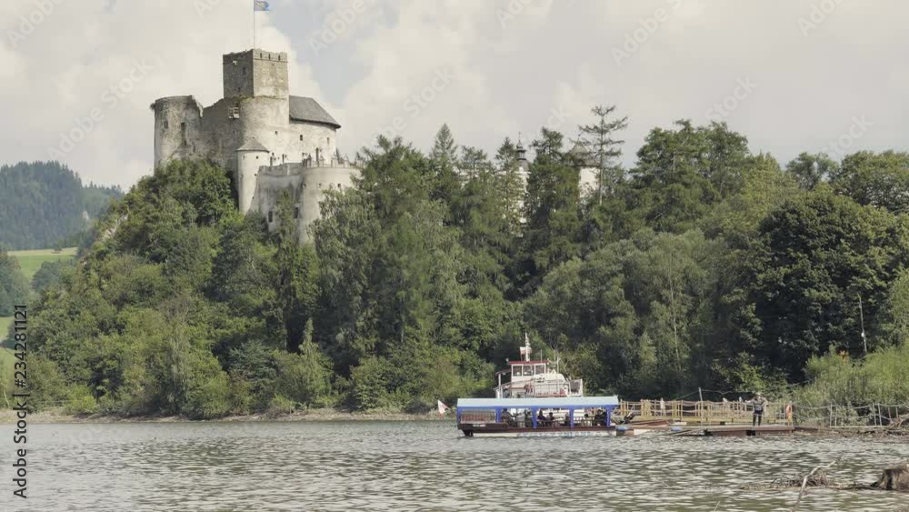 Medieval castle on hill above lake. Lake with ferry, tourist boat. Monumental stone historic building with large tower. Summer holiday scenery with clouds. Positive mood, beautiful landscape Medieval castle on hill above lake. Lake with ferry, tourist boat. Monumental stone historic building with large tower. Summer holiday scenery with clouds. Positive mood, beautiful landscape