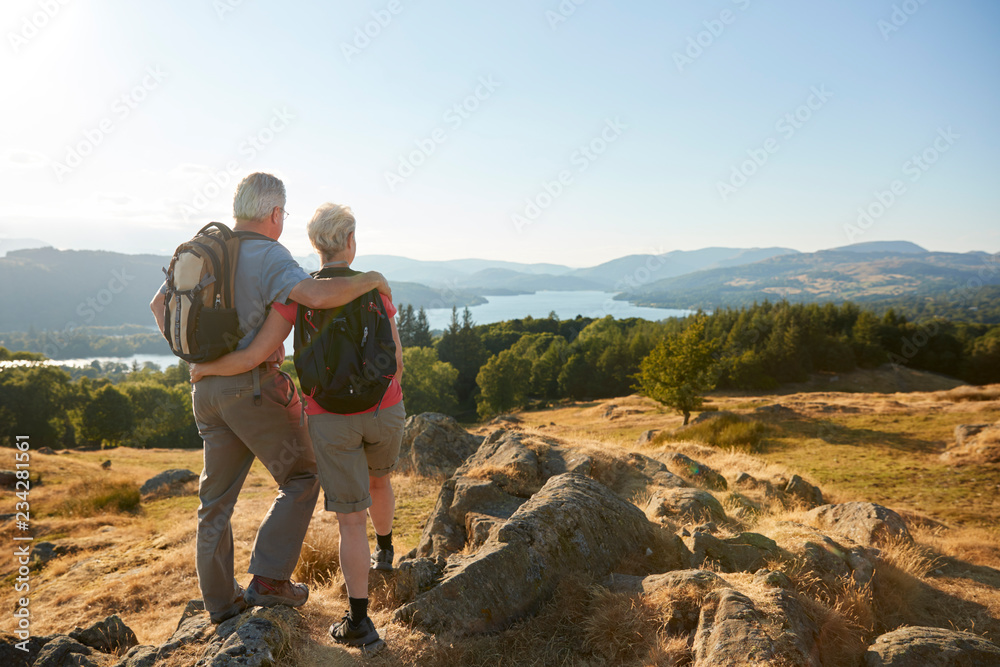 Rear View Of Senior Couple Standing At Top Of Hill On Hike Through Countryside In Lake District UK