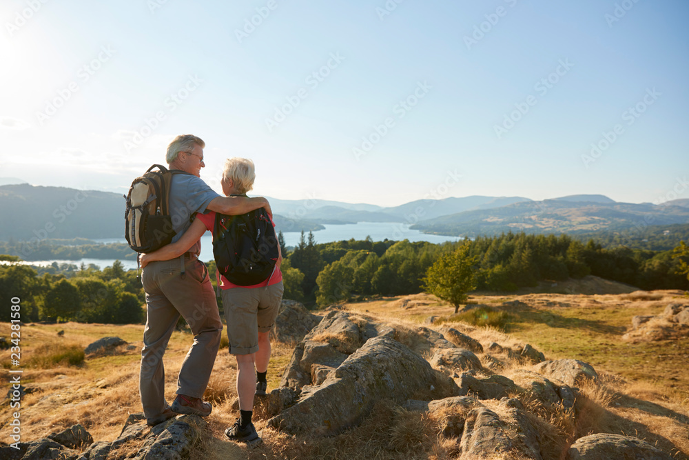 Rear View Of Senior Couple Standing At Top Of Hill On Hike Through Countryside In Lake District UK