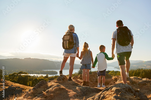 Fototapeta Rear View Of Family Standing At Top Of Hill On Hike Through Countryside In Lake