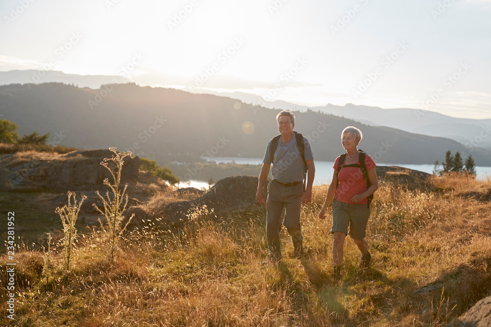 Senior Couple Walking On Top Of Hill On Hike Through Countryside In Lake District UK