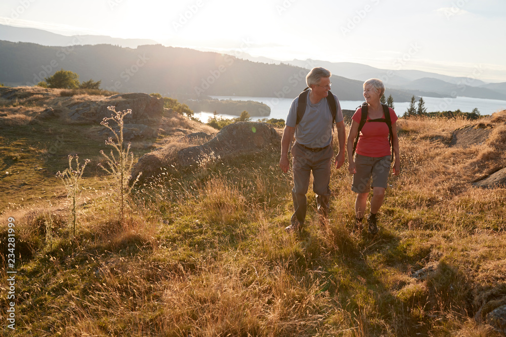 Senior Couple Walking On Top Of Hill On Hike Through Countryside In Lake District UK