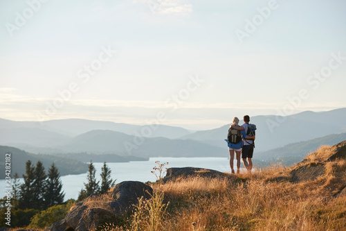 Fototapeta Rear View Of Couple Hugging On Top Of Hill On Hike Through Countryside In Lake D