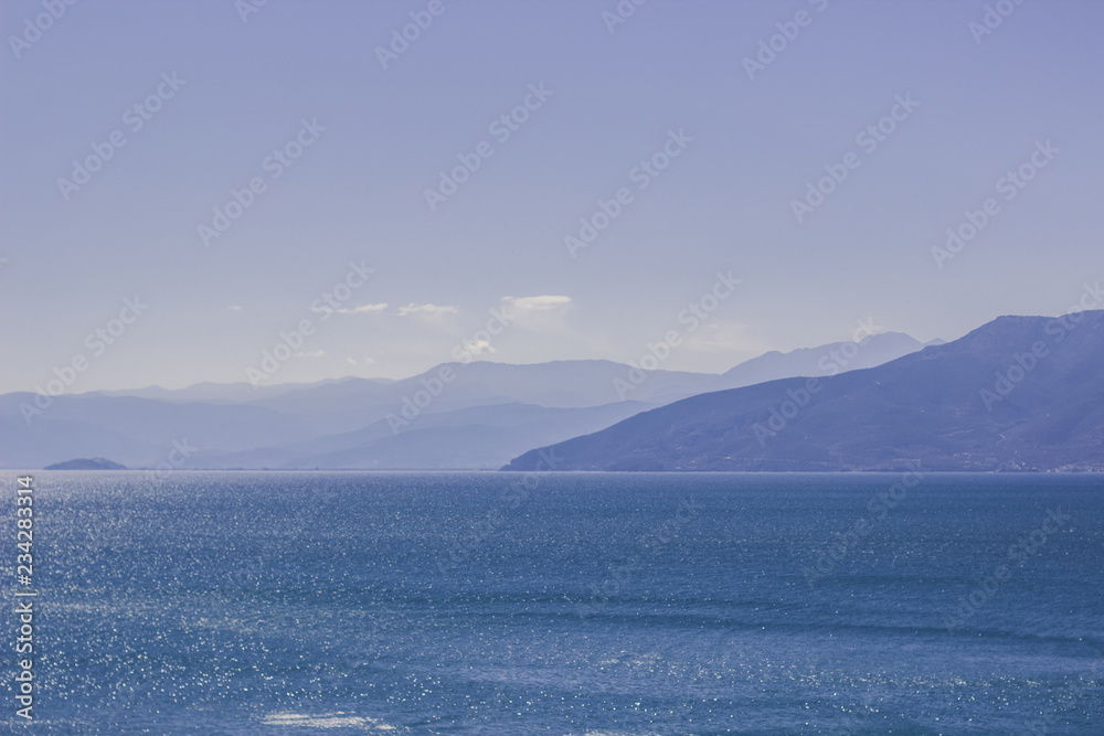 abstract morning mystic and atmospheric nature landscape of sea bay calm water surface and mountain horizon background silhouettes in foggy weather time