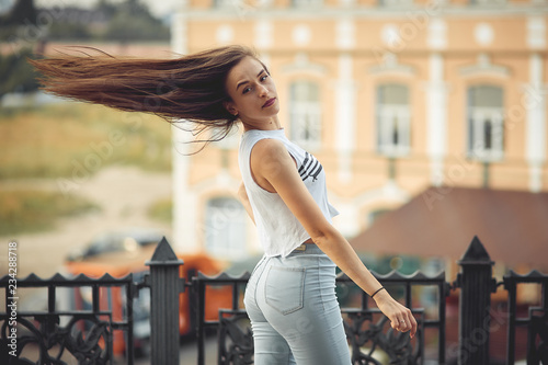 portrait of a girl in jeans and a t-shirt on the background of the building in the evening on a summer day. street dancing in the city photo