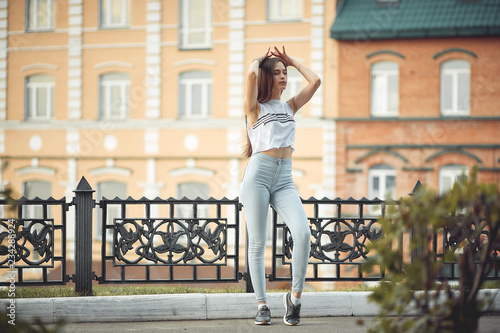 portrait of a girl in jeans and a t-shirt on the background of the building in the evening on a summer day. street dancing in the city photo