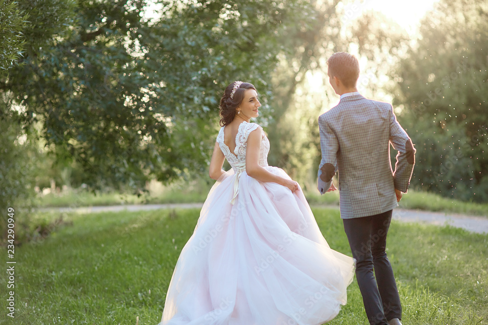 Just married loving hipster couple in wedding dress and suit on green field in a forest at sunset. happy bride and groom walking running and dancing in the summer meadow. Romantic Married young family