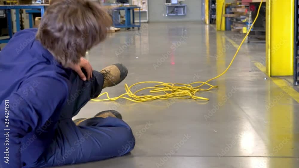 A young factory worker trips over an electrical cord in an industrial plant