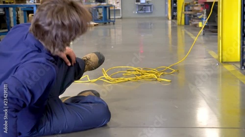 A young factory worker trips over an electrical cord in an industrial plant
