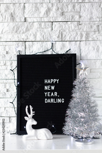 Happy new year darling words made with white letters on a black board with Christmas tree on  white brick wall background