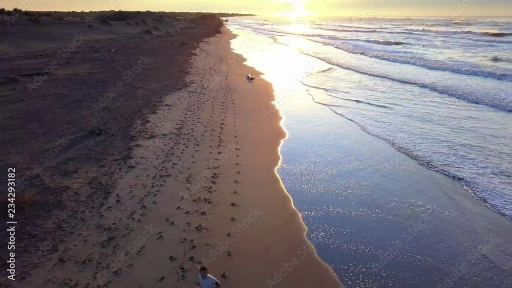 Dynamic aerial view descent with drone on young attractive man jogging on the beach at sunrise. Running workout practice in fitness and healthy lifestyle concept.