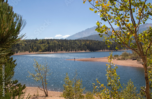 Fototapeta Naklejka Na Ścianę i Meble -  Sunshine sparkles on the water a fisheman stands on a point and aspen leaves turning yellow shimmer at Chrystal Reservoir half way up Pikes Peak mountain near Colorado Springs