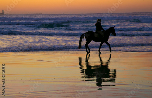 femme sur un cheval sur la plage au coucher du soleil