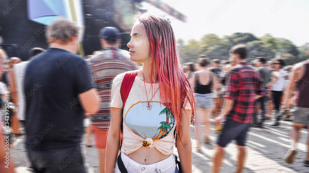 Young beautiful tenager, pink hair, informal appearance, at a concert in a crowd of people, waiting for performance by favorite singer. World scale music festival. Mass event, happy moments of life