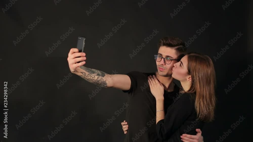 Portrait of two happy lovers making selfie on smartphone on black background. Happy hipster couple taking a selfie on black background. Portrait of two happy lovers making selfie on smartphone on black background. Happy hipster couple taking a selfie on black background.