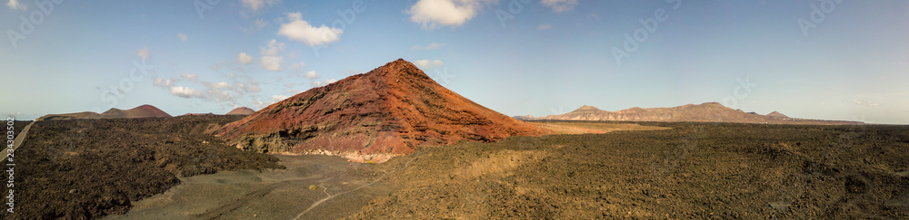 Vista aerea della montagna Bermeja di un color rosso intenso, circondata da campi di lava. Strada costiera che attraversa la lava nera e piccolo lago. Lanzarote, Isole Canarie, Spagna