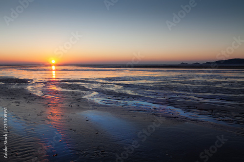 Sunrise over Swansea Bay on a low tide, showing Mumbles lighthouse and pier, South Wales, UK