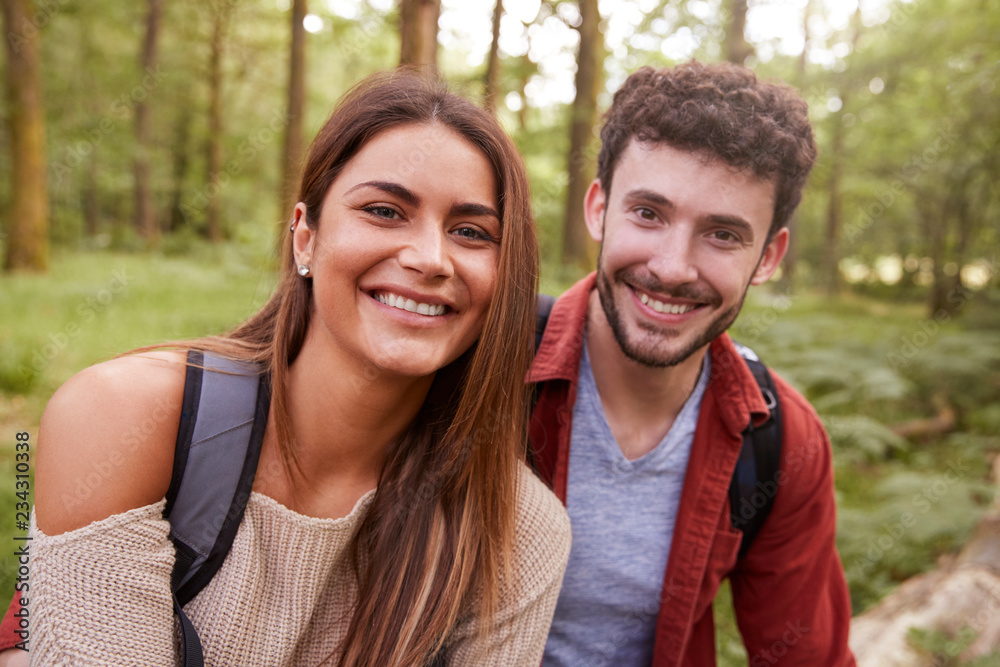 A young adult couple smiling to camera during a hike in a forest, close up portrait