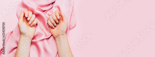 Beautiful woman manicure on creative trendy pink background with silk fabric. Minimalist manicure trend. Top view, flat lay. Copy space for your text.