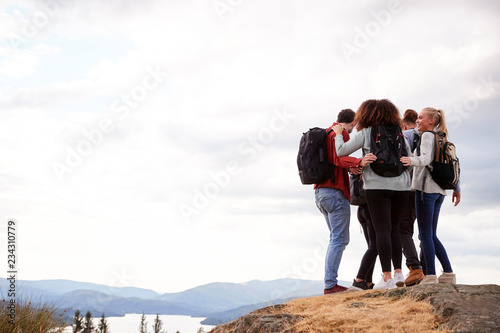 A group of five mixed race young adult friends embrace after arriving at the summit during mountain hike, close up