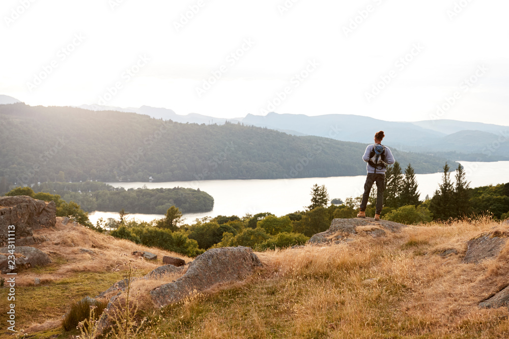 A young mixed race man standing alone on rocks, admiring lake view, back view
