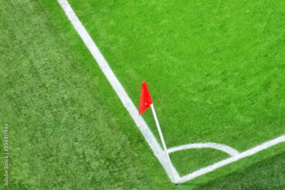 Fototapeta premium Blurry of green soccer field.Beautiful grass on the stadium.Abstract football ground background with white stripe line and red flag on the corner.Background,Sport,Texture Concept