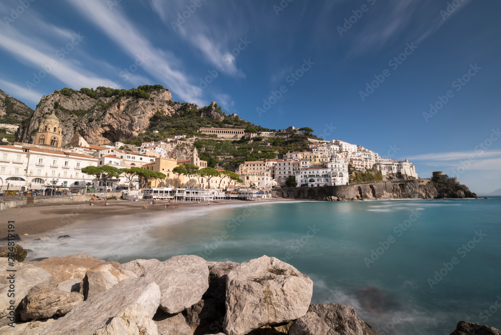 Amalfi coast with nice white houses and beach with blurred turquoise water and breakwater foreground, Italy. Long exposure