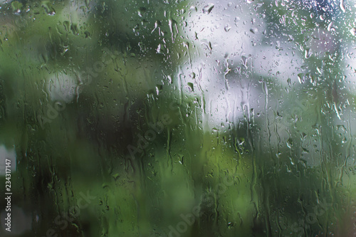 window glass with dripping raindrops and blurred background